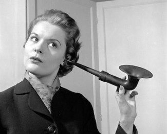 Schwarzweiss-Foto einer Dame, die konzentriert in ein Hörrohr horcht